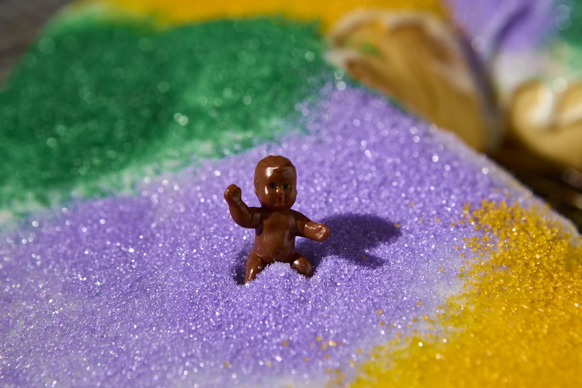 A close-up for a brown toy plastic baby sitting on a cake.