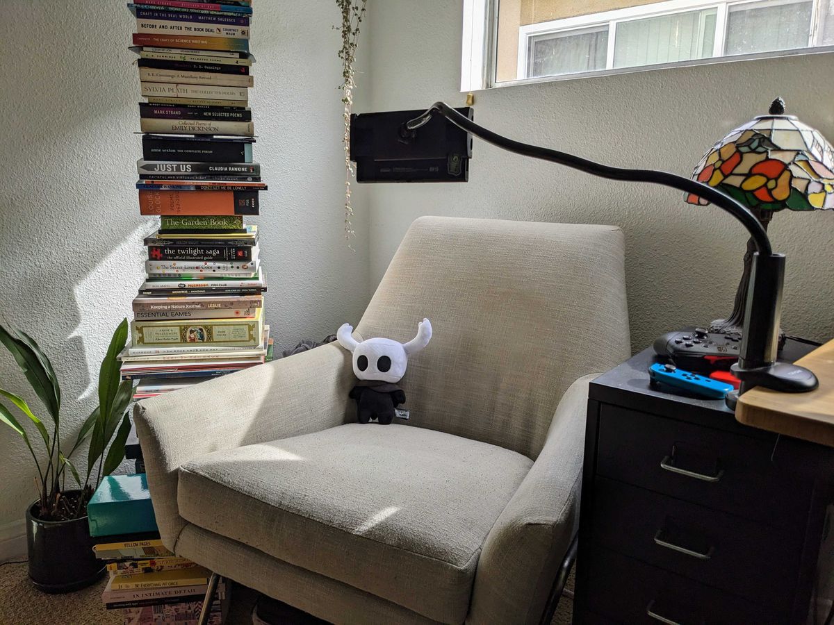 A tablet mount is holding a Nintendo Switch facing an armchair. A Hollow Knight plush sits in the chair.