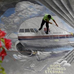 In this April 8, 2014 file photo, a school utility worker mops a mural depicting the missing Malaysia Airlines Flight 370, at the Benigno "Ninoy" Aquino High School campus at Makati city east of Manila. After a calamitous year for aviation, hundreds of government and industry officials will gather in Montreal this week in an attempt to reach a consensus on how to prevent any more airliners from disappearing without a trace or being shot down while flying over a conflict zone.