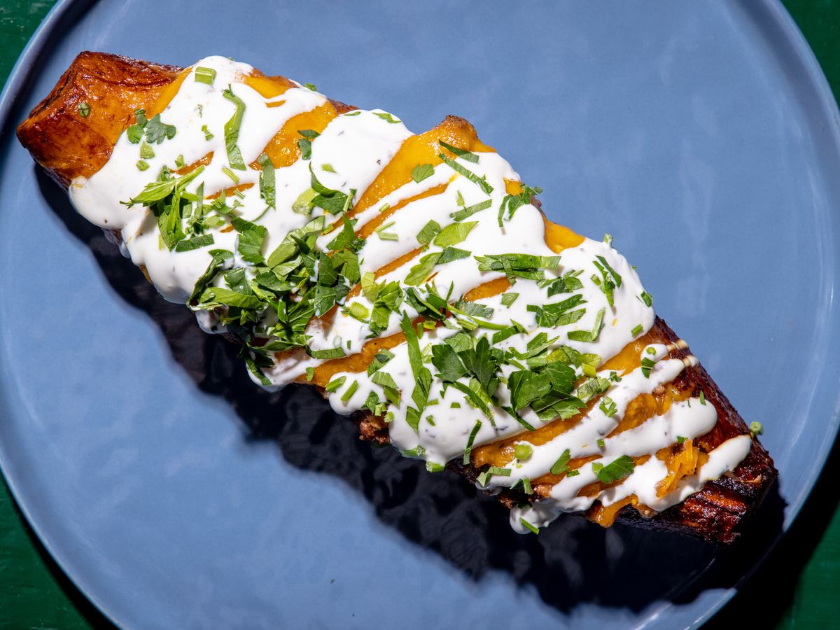 A long, chubby, lamb-stuffed plantain is shot from overhead; white labneh sits on top in a squiggly pattern, while cilantro provides a green hue