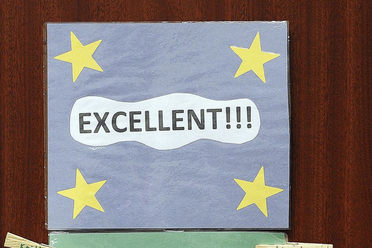 A pale blue poster proclaiming “Excellent!!!” with four yellow stars in the corners hangs on a wall.
