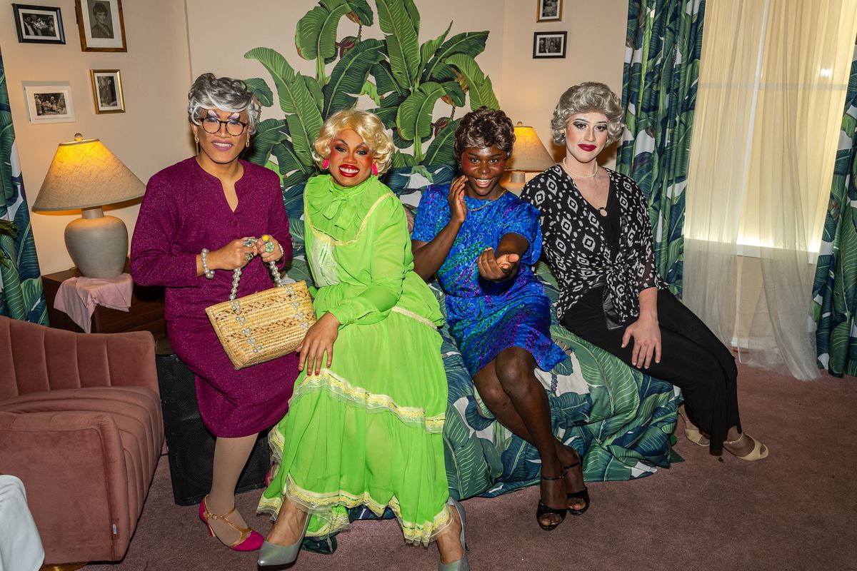 A group of four drag performers dressed as the “Golden Girls” pose on a replica of the TV show set.
