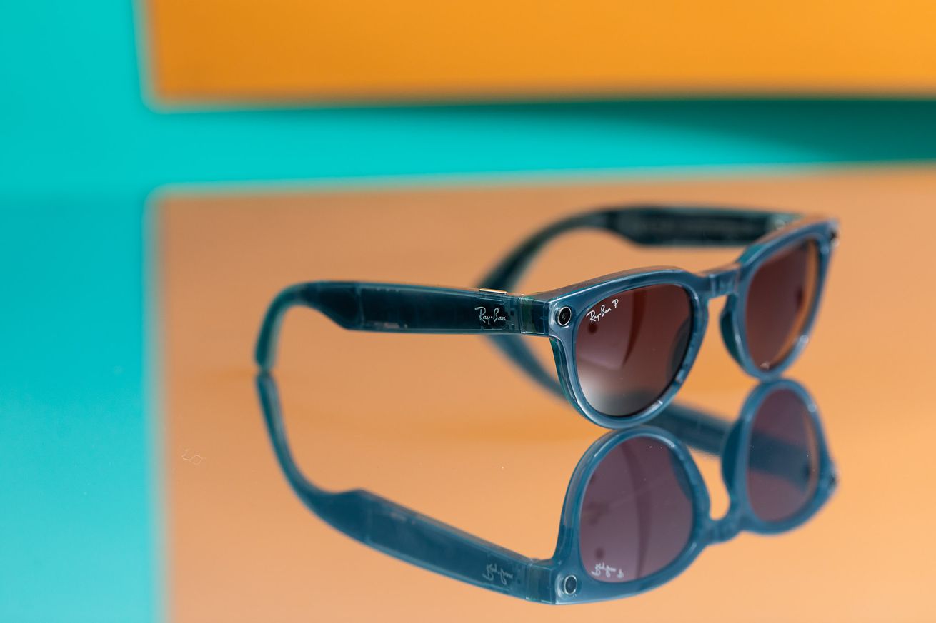 Blue Ray-Ban Meta Smart Glasses with pinkl enses on a colorful mirror.