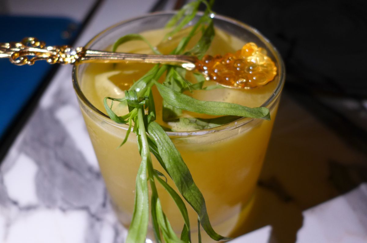 A cocktail witha gilt spoon poised on top with a sprig of tarragon.