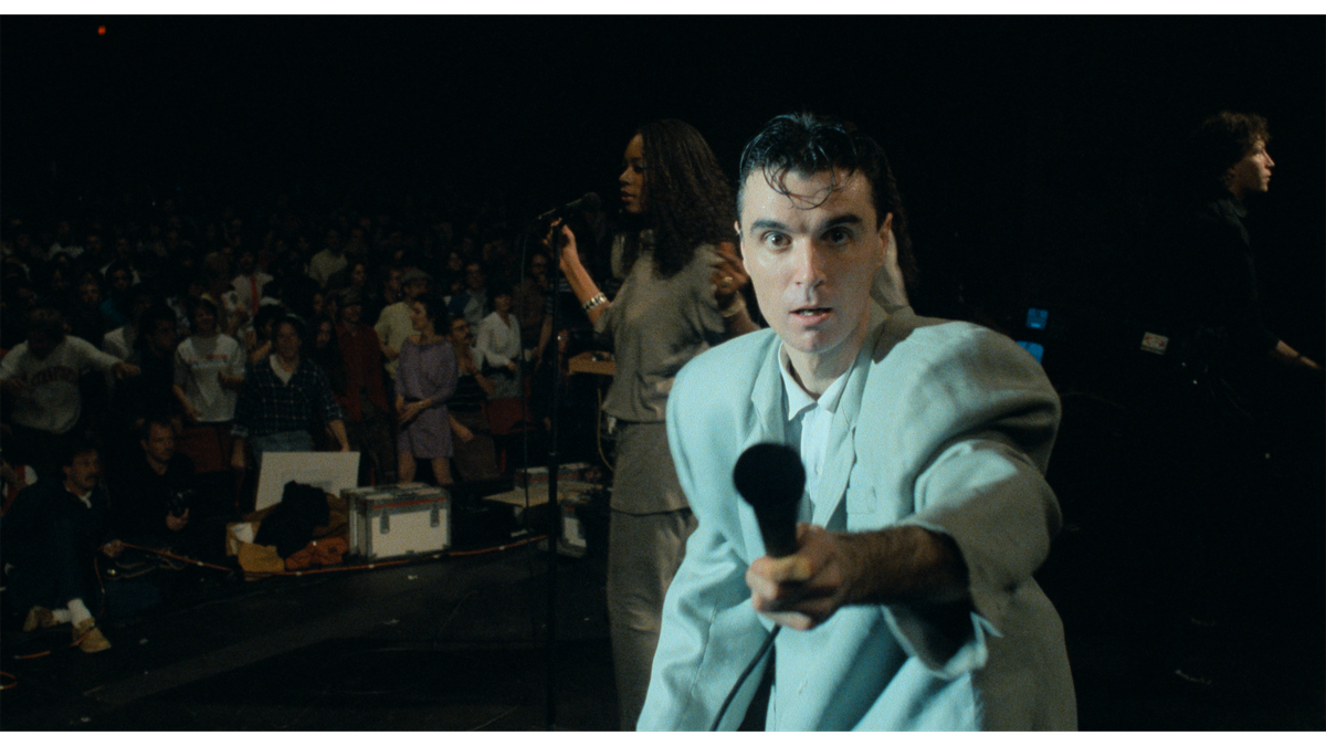 David Byrne, wearing his signature suit, holds the microphone towards the camera in Stop Making Sense.