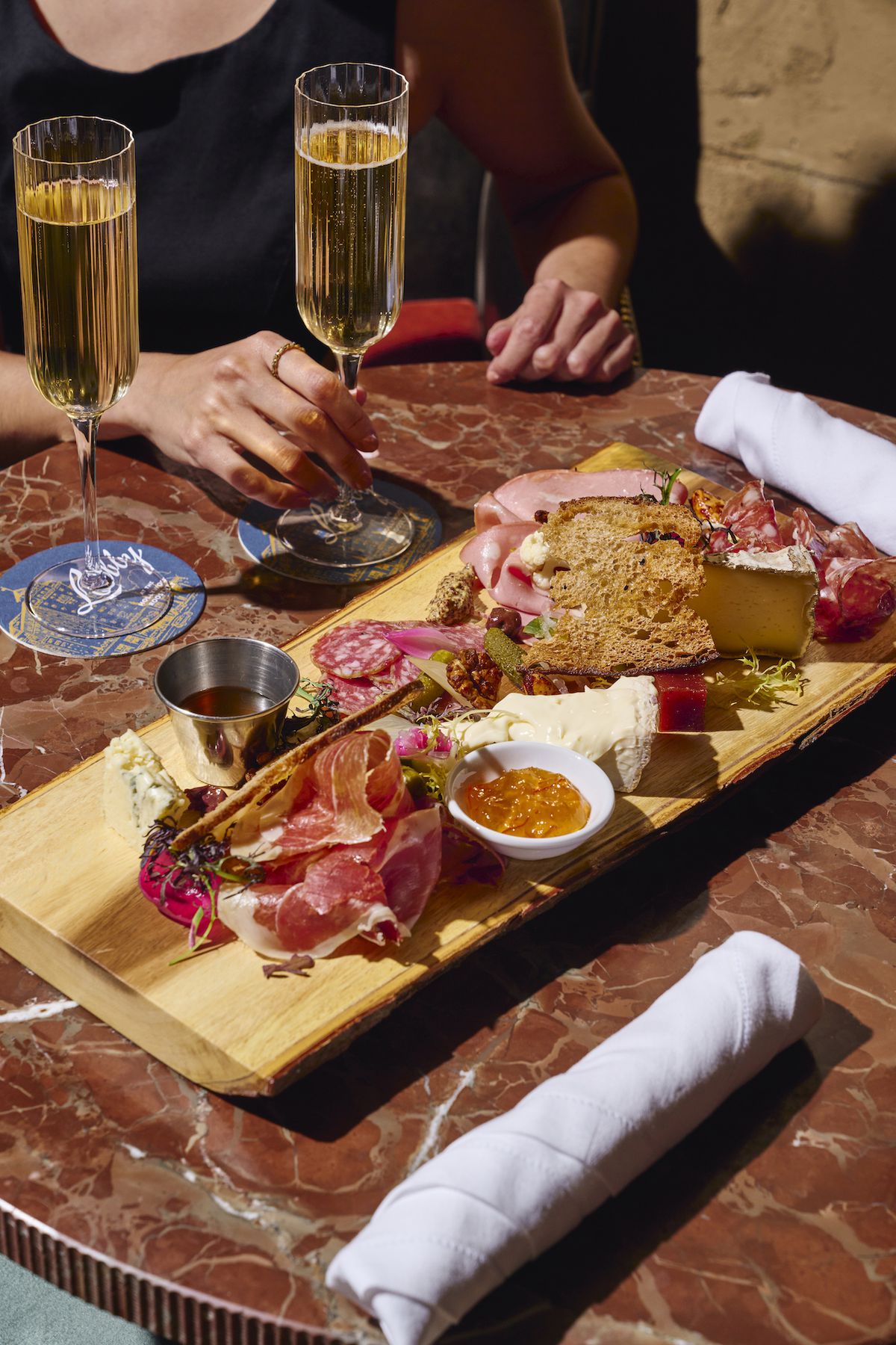 A deep red marble table holds a wooden platter of cured meats and cheese from new restaurant Shirley Brasserie.