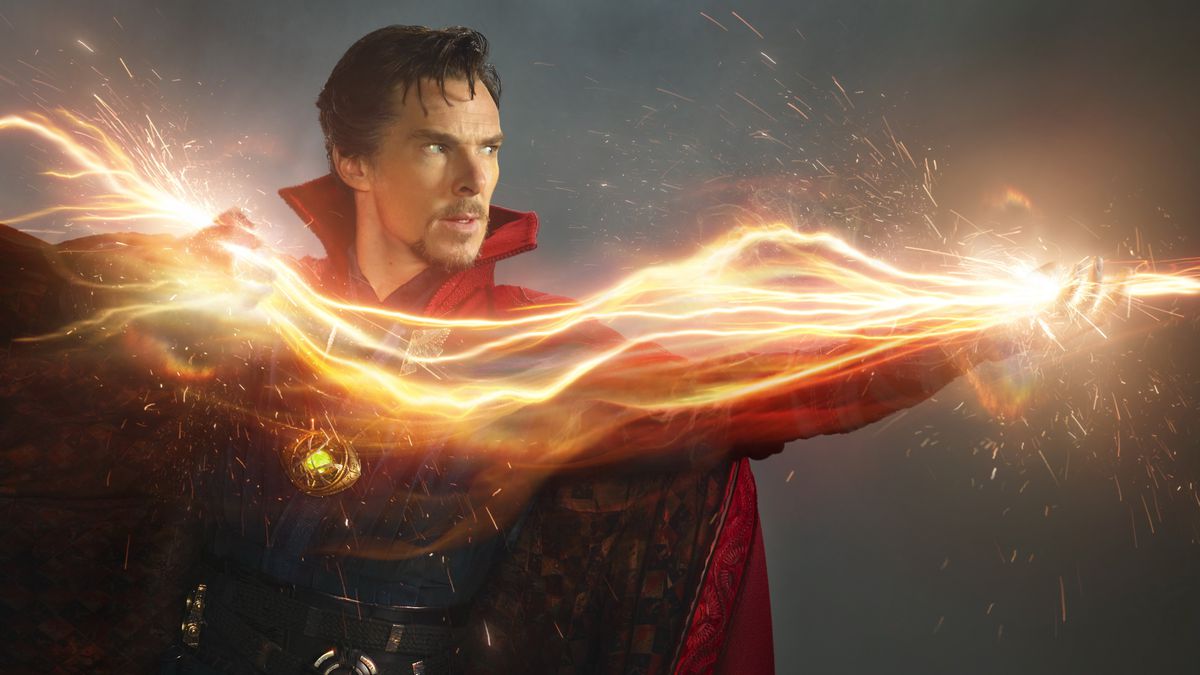 Benedict Cumberbatch as Doctor Strange, in a publicity photo showing him in front of a neutral background, zapping something offscreen with a huge wave of bright orange magical energy