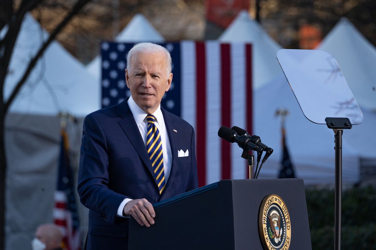 Joe Biden standing outdoors at a lectern, with a U.S. flag behind him