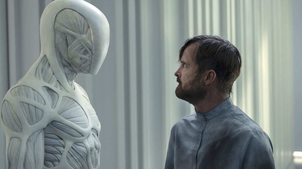 A spindly muscular white robot stands face to face with a white bearded man in a hospital gown in Westworld season 4
