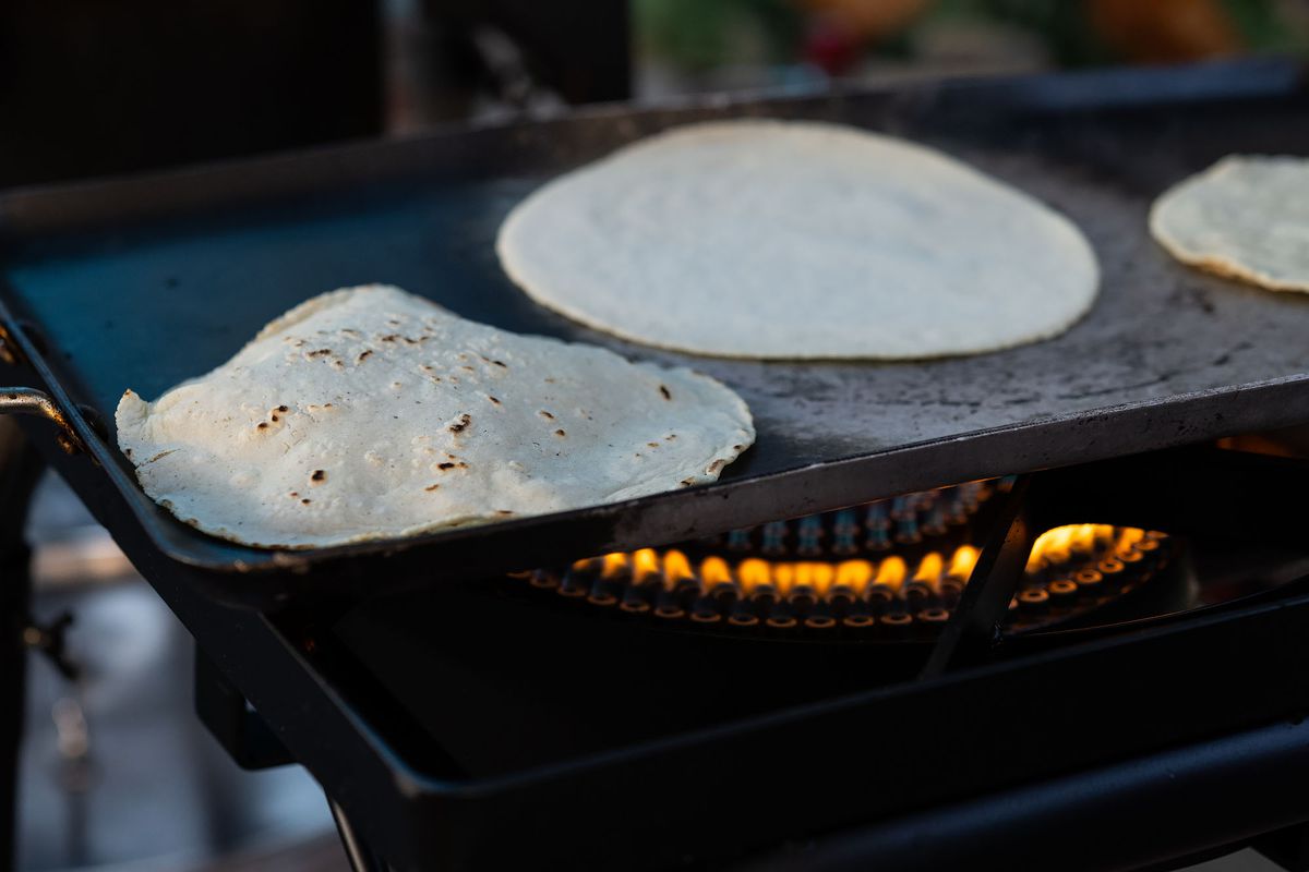 Tortillas on a comal with a burning flame underneath.
