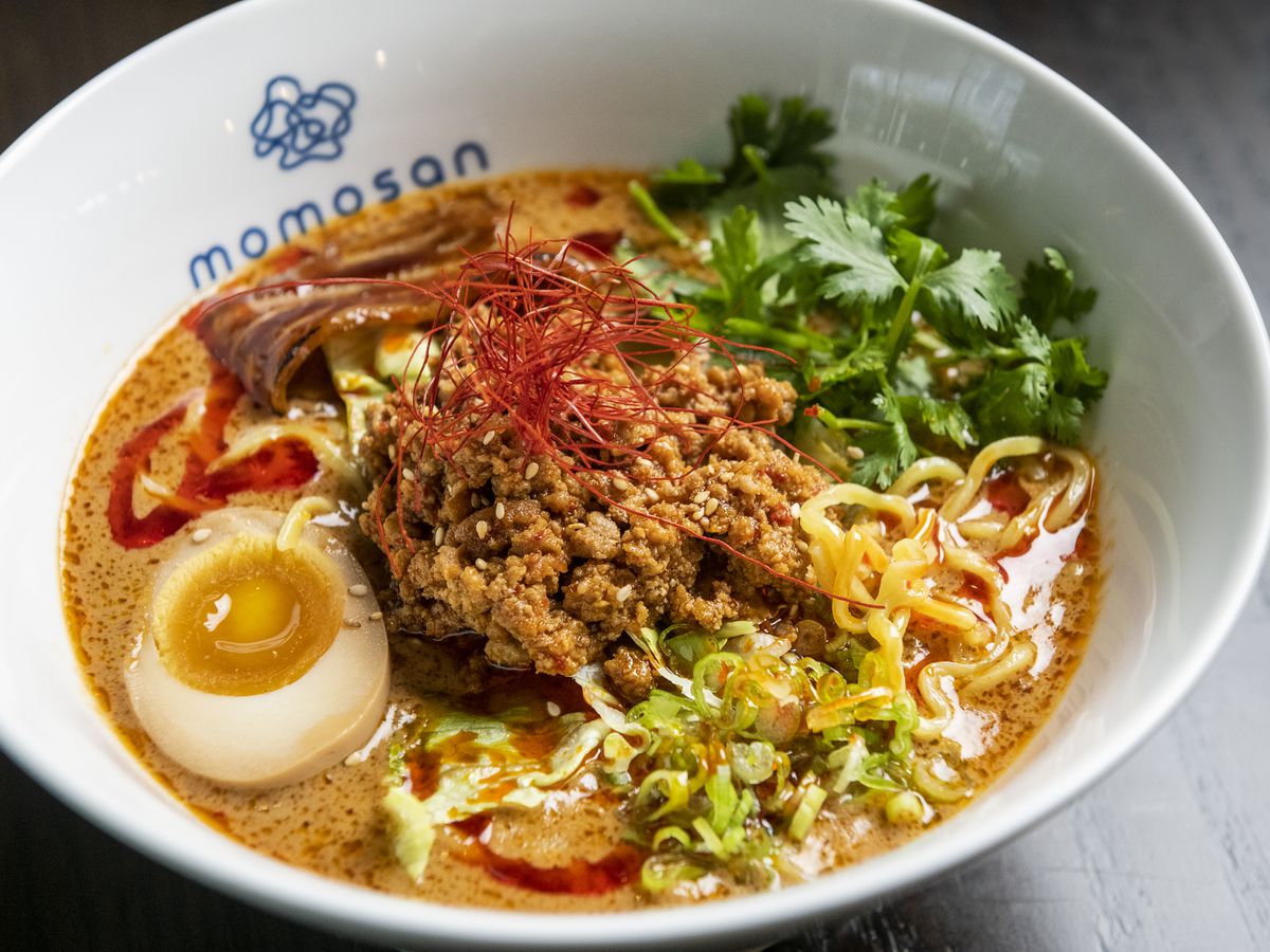 Closeup shot of a bowl of ramen with ground pork, a thick yellow-orange broth, a runny egg, and other toppings.