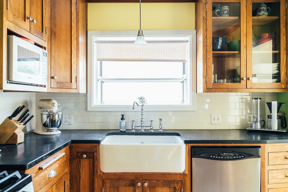 An open kitchen with a large farmhouse sink and dark counters. There is a window over the sink.