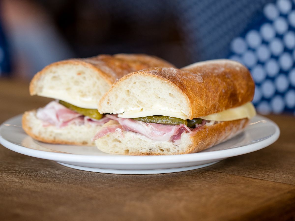 Ham, salted butter, Comté cheese, cornichons on a baguette sitting on a plate.