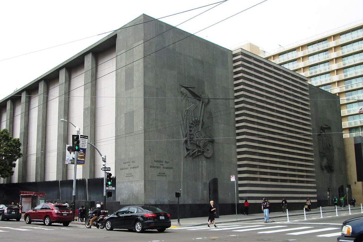 A massive corner substation building, a low, gray cement building behind a black fence.