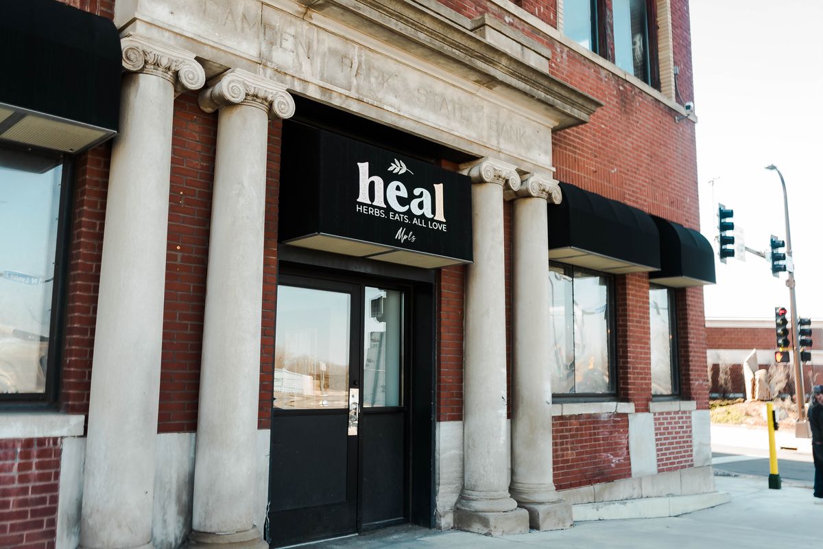 A red brick building with concrete columns and black awnings, the center awning with a white sign that says “heal” in block letters.
