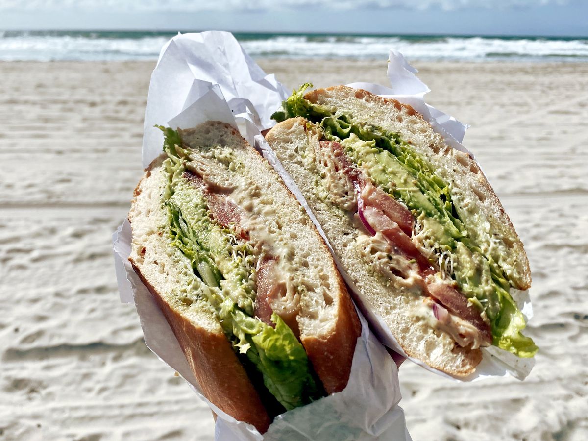 Veggie filled sandwich held up in front of the Pacific Ocean.