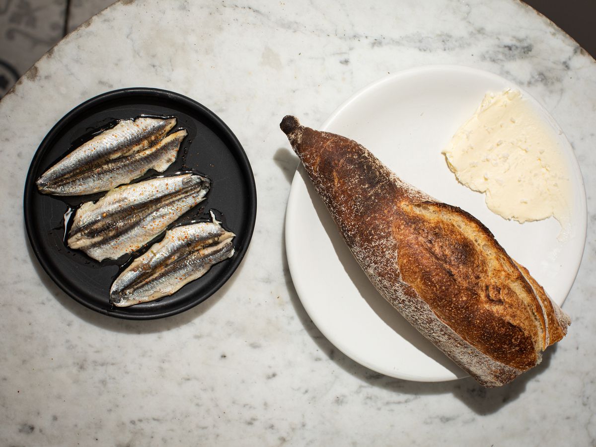 An overhead photograph of two plates, one with three fish filets and another with a baguette and smear of butter