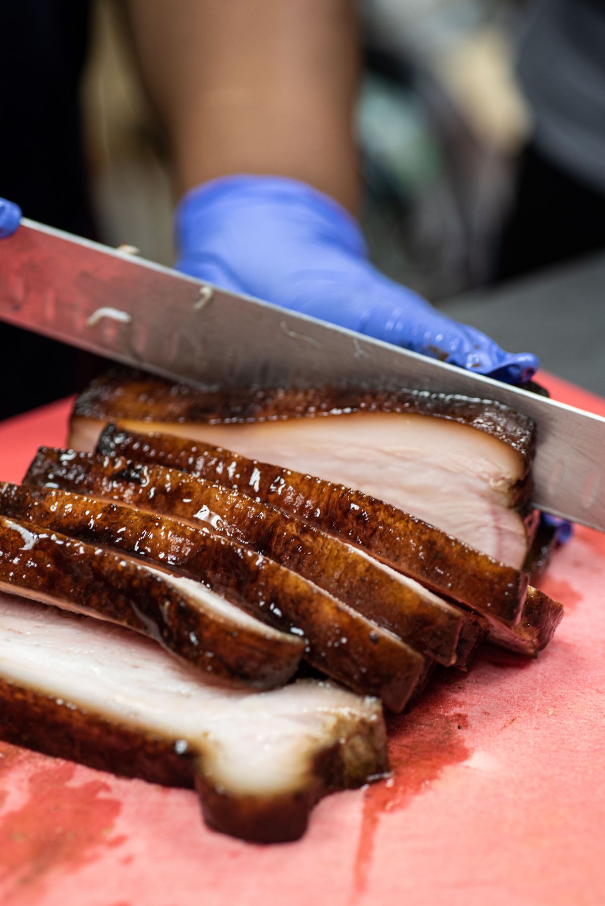 A broad knife cuts thick slices of pork belly.