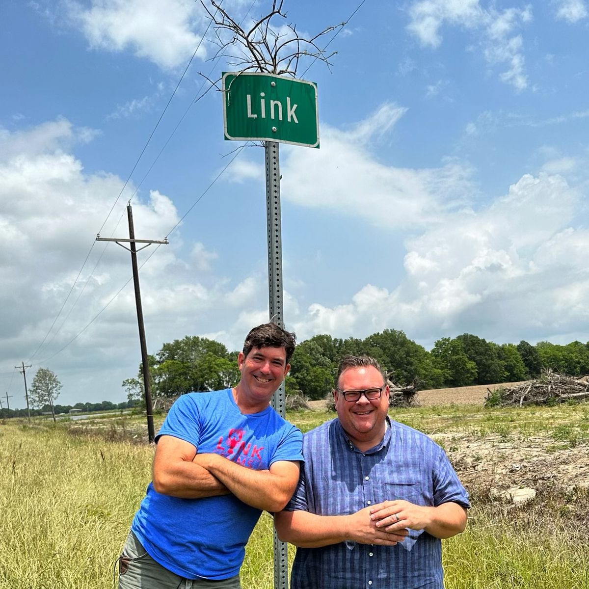 Chris Shepherd and a man stand in front of a sign that says Link in Louisiana while filming a segment for TV segment “Eat Like a Local.”