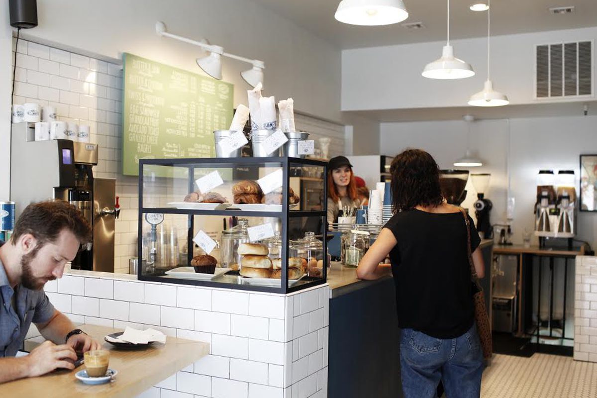 A coffee shop with white subway tiles and customers near a counter.