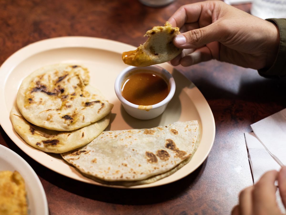 A plate of pupusas with sauce and a hand reaching for some food