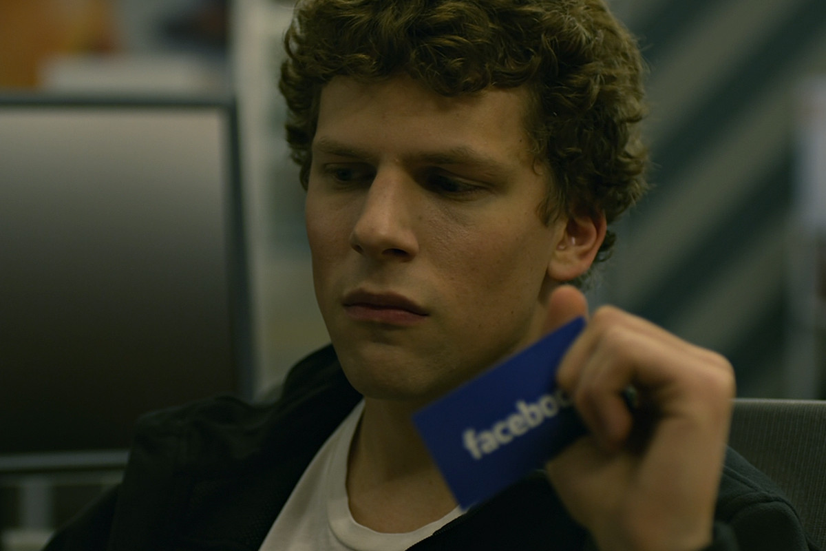 jesse eisenberg’s mark zuckerberg contemplates his business in a spinny chair while holding a Facebook business card in The Social Network