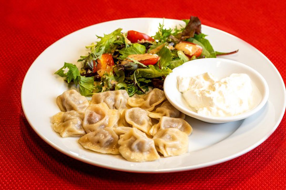A plate of steamed little dumplings served with sour cream and a green salad.