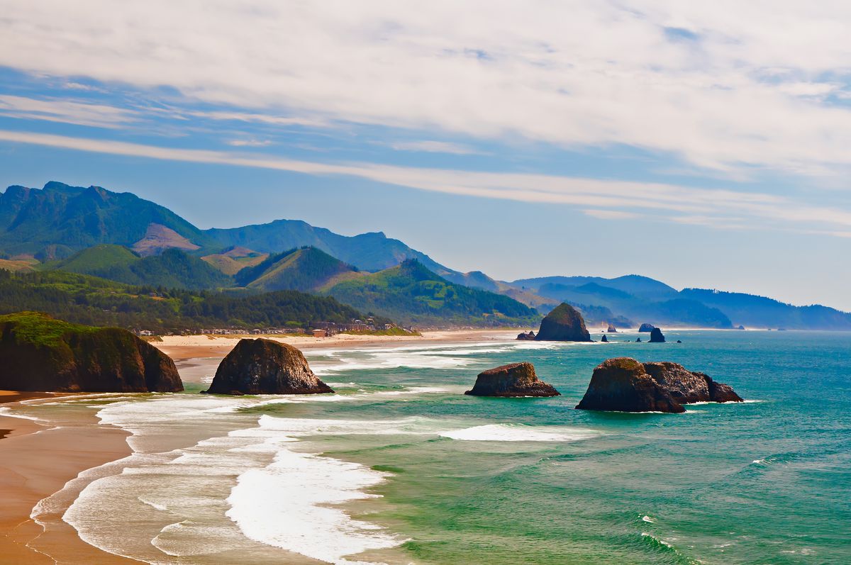 Cannon Beach in Oregon. In the foreground is a body of water and a beach. In the distance are mountains.