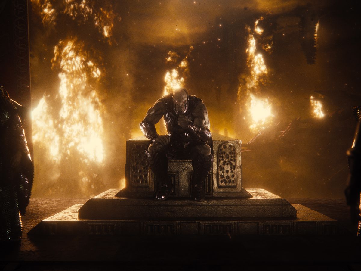 The alien villain Darkseid sits on a throne in a burning room in Zack Snyder’s Justice League