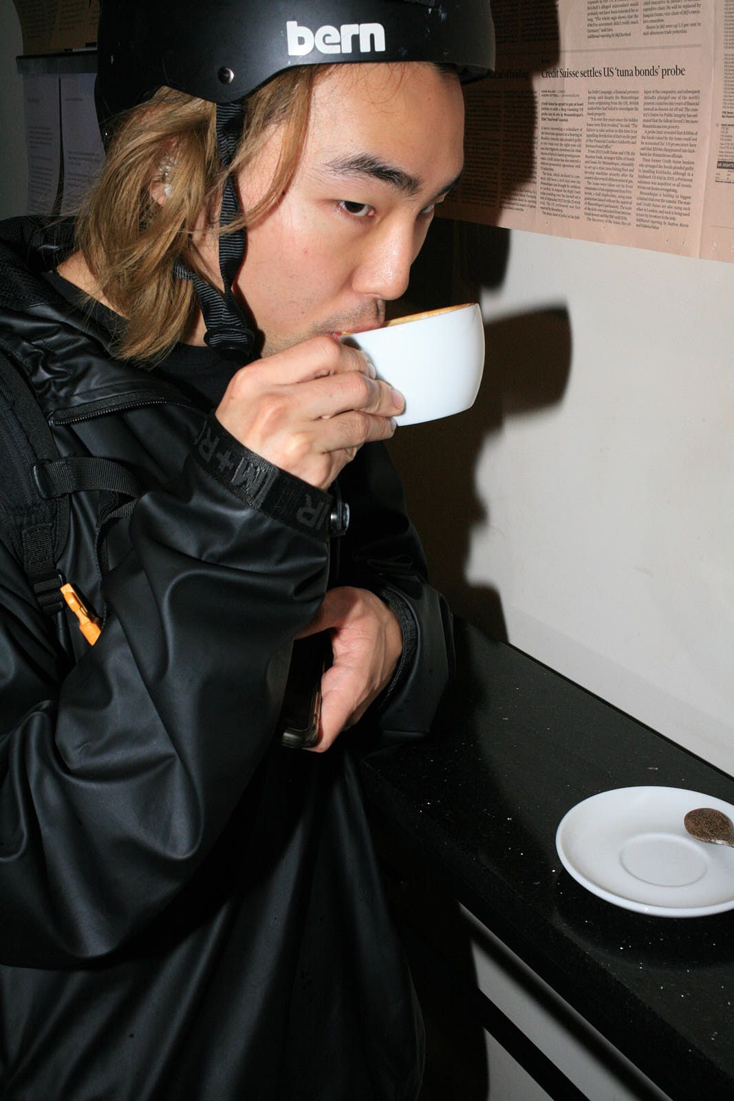 A man in a bike helmet with long blonde hair sips a coffee from a white ceramic cup.