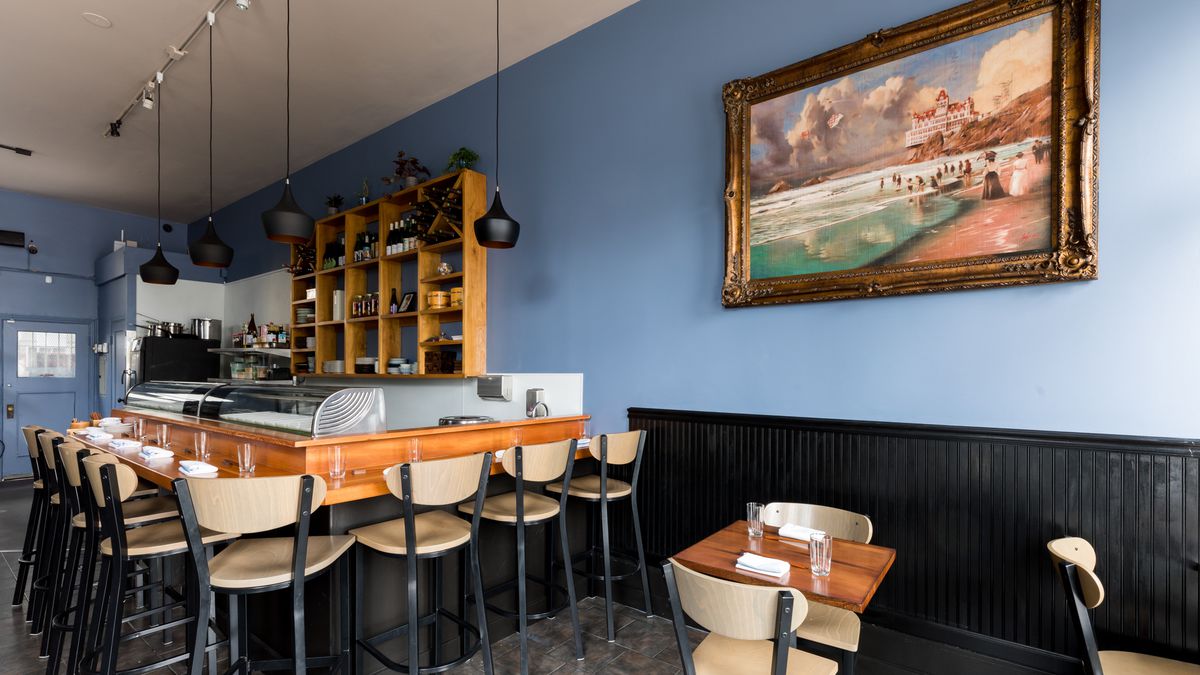 Inside Chisai Sushi Club, a small restaurant on Mission Street with blue walls and a warm wooden sushi bar with seats for 8 diners. A customer painting of Ocean Beach hang on one wall. 