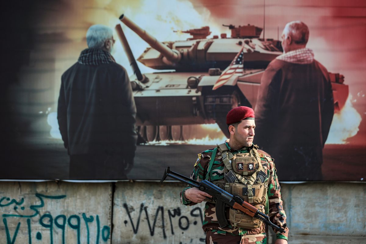 An armed soldier in front of a poster depicting a burning tank adorned with an American flag.