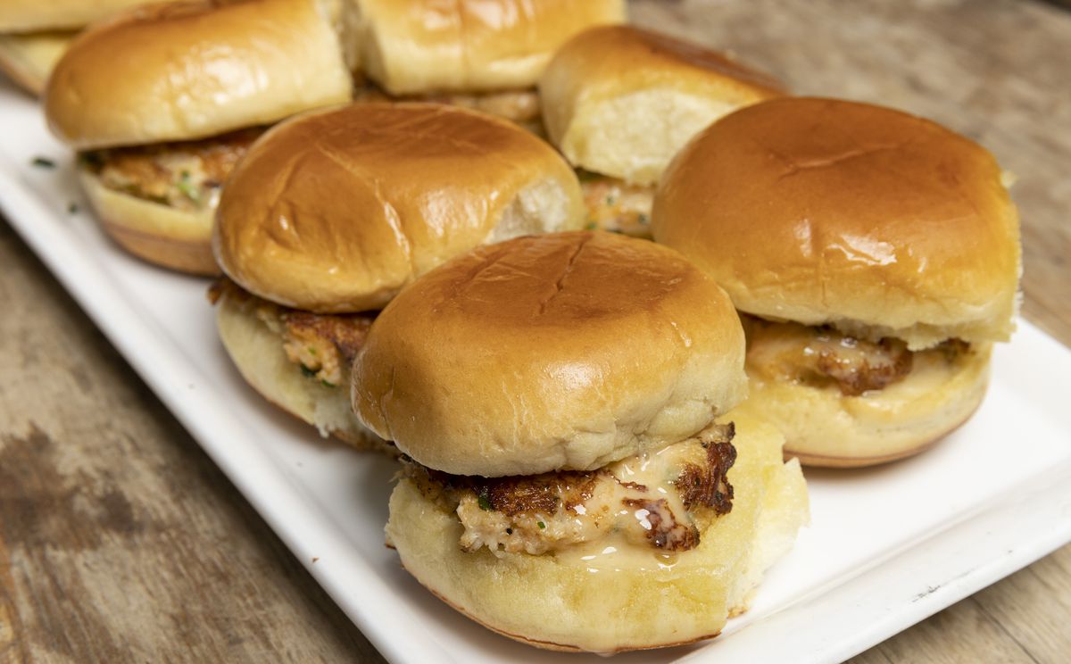 A rectangular white plate of chicken sliders on buns. 