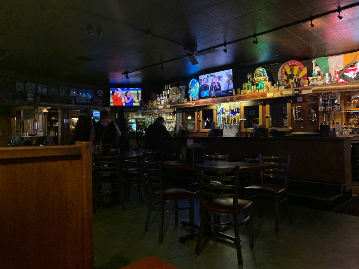 People sit at a dimly lit bar with TVs playing in the background.