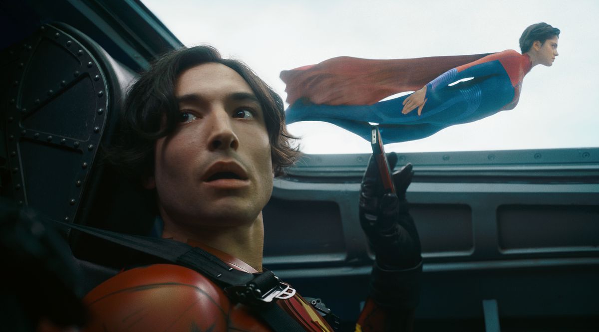 Ezra Miller as Young Barry looks goofy as he takes cell phone video of Sasha Calle’s Supergirl flying by the plane he’s in in The Flash.