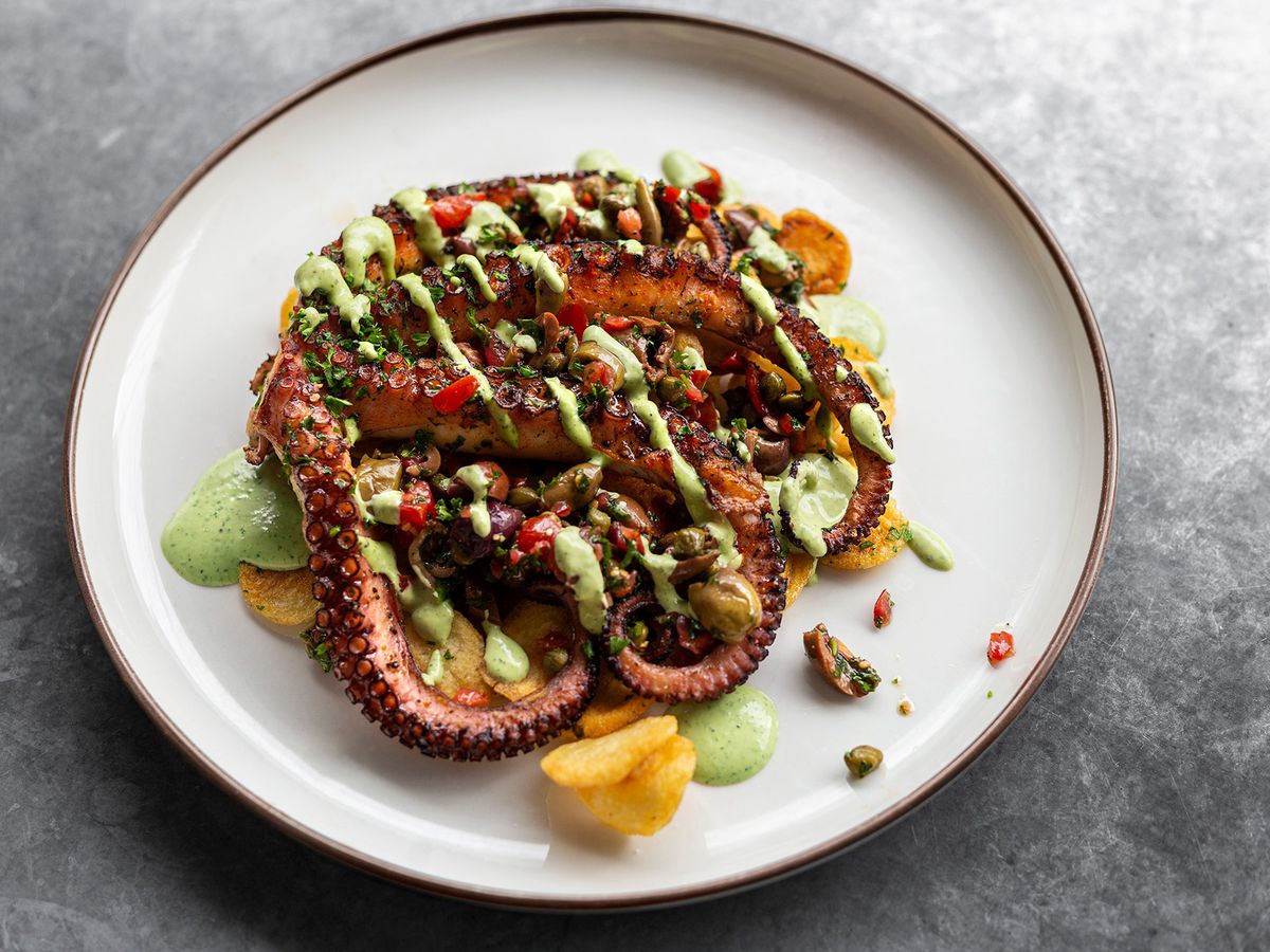 From above, octopus tentacles splayed on a plate with diced vegetables and green sauce drizzled over top
