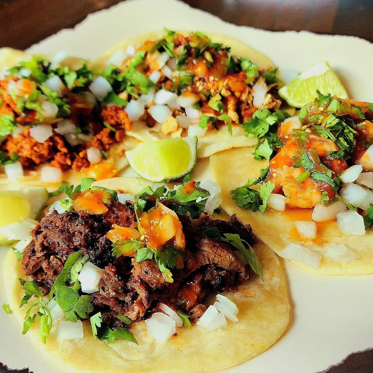 Four street tacos with al pastor, chorizo, shrimp, and carne asada dressed with cilantro and onions and squeezes of lime. 
