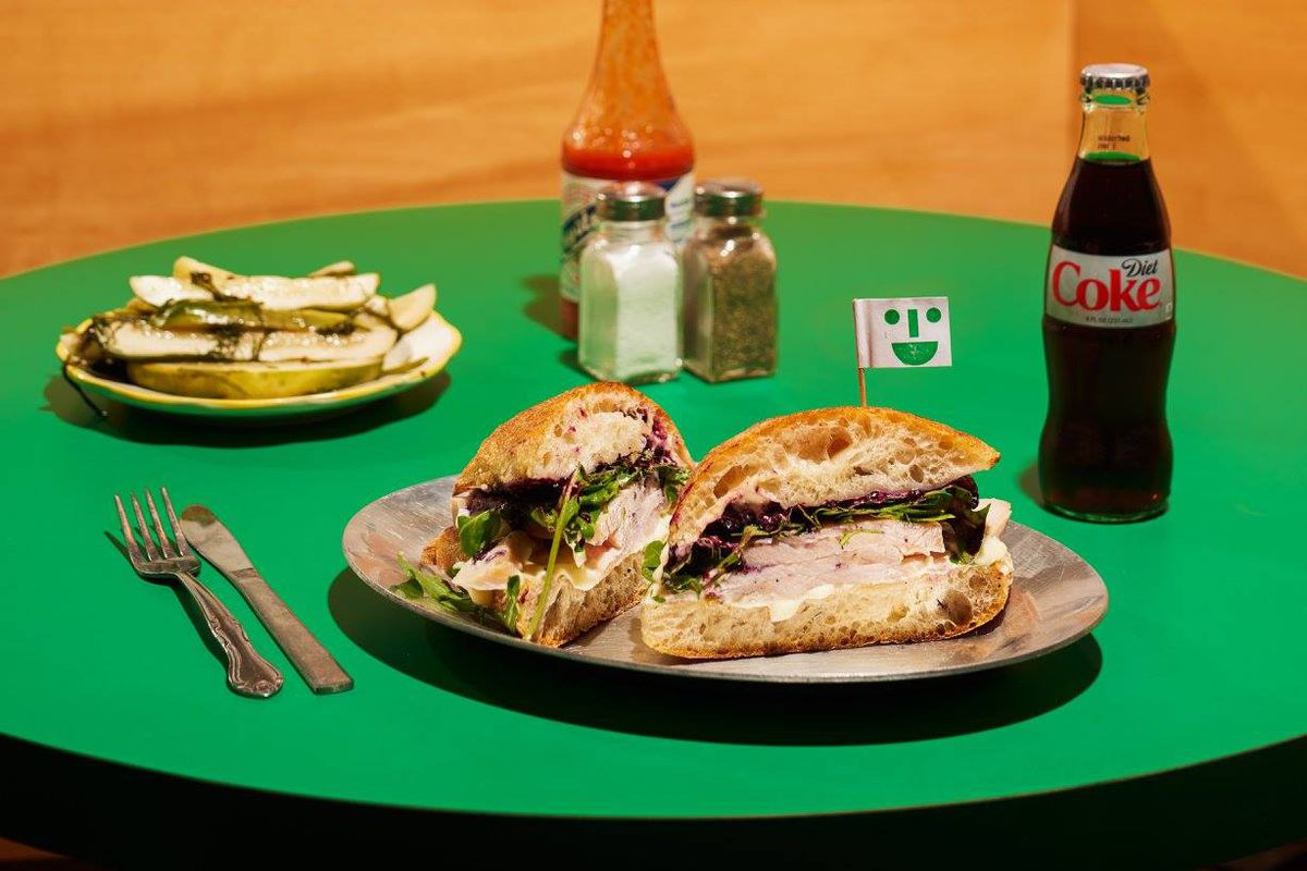 a green table with middle child turkey sandwich, pickles, a coke and place settings