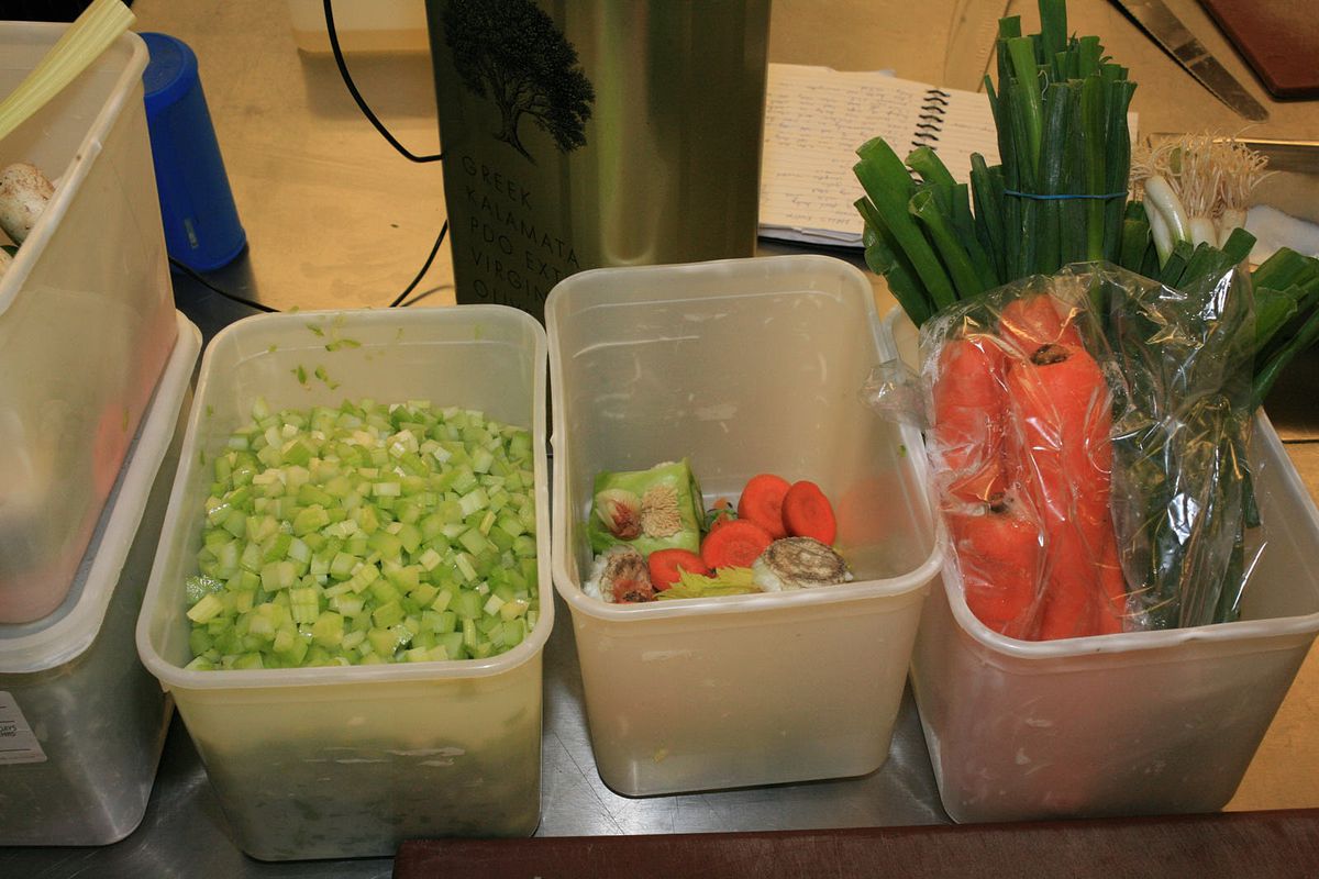 Three plastic containers, filled from left-to-right with diced celery; roughly chopped carrots, mushrooms, and celery; and sheaths of spring onions and carrots