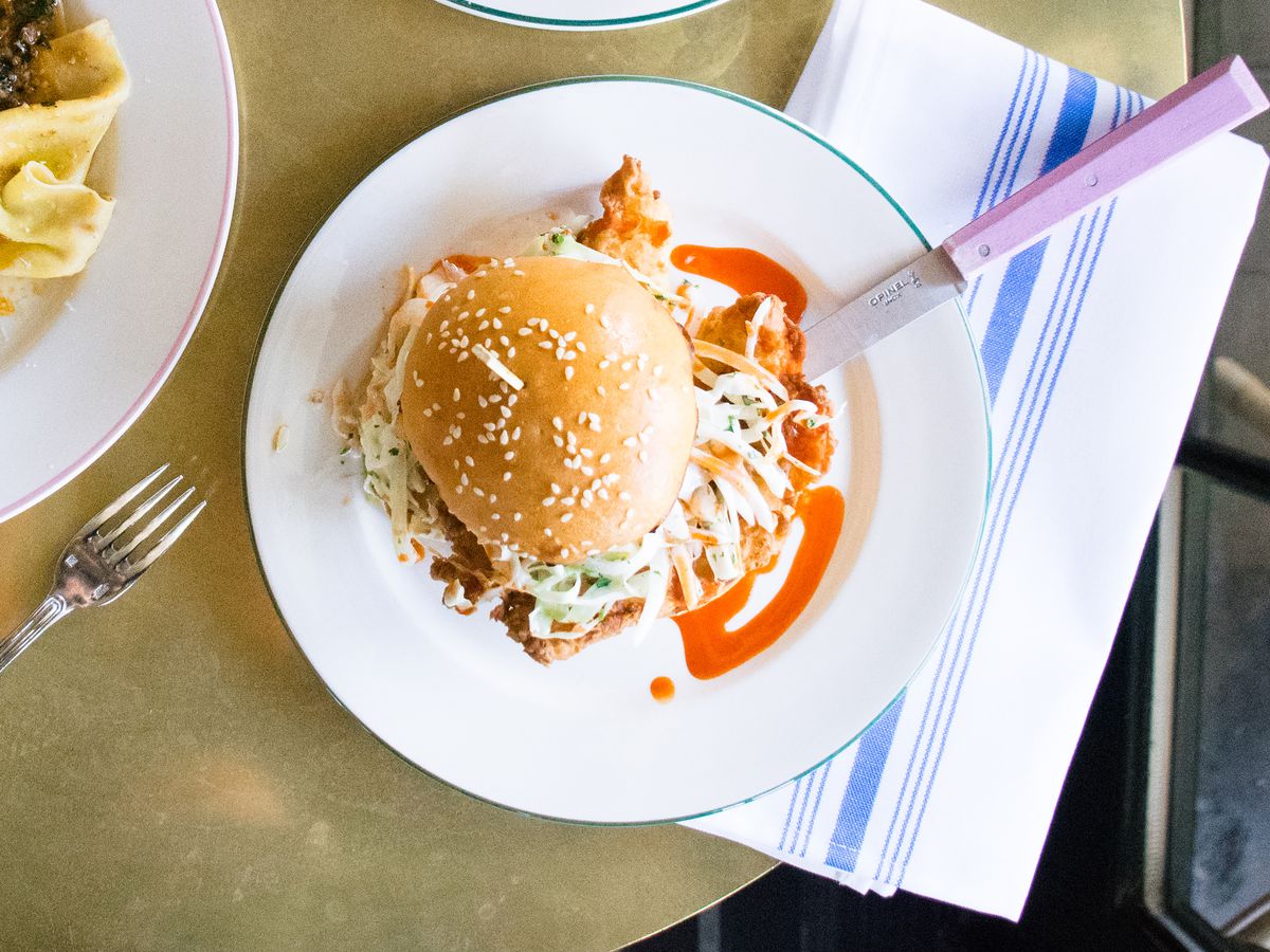 A fried chicken sandwich seen from above on a plate with hot sauce drizzles.