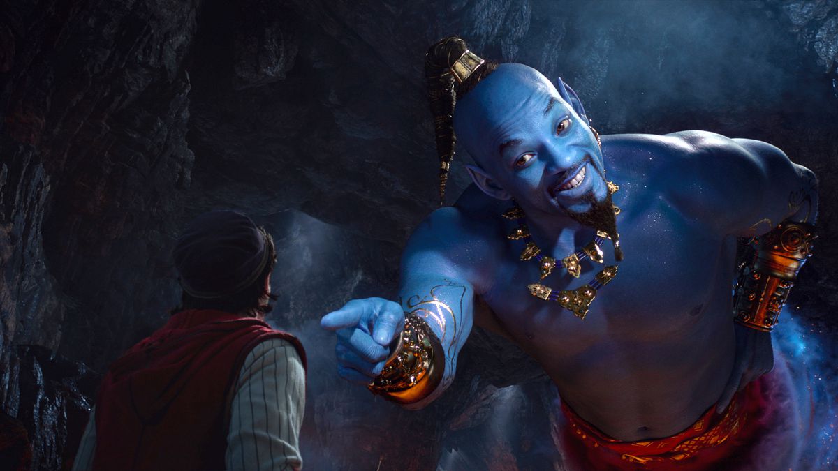 Genie (Will Smith, in blue paint, shaved head with topknot, and gold necklace and wrist cuffs, gives a big grin to Aladdin in the 2019 live-action Aladdin remake