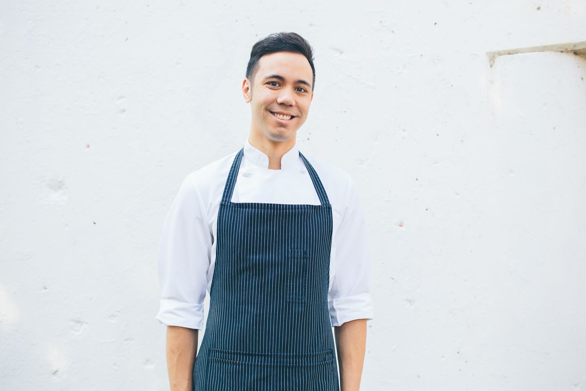 A chef in a white shirt with a dark apron who is smiling.