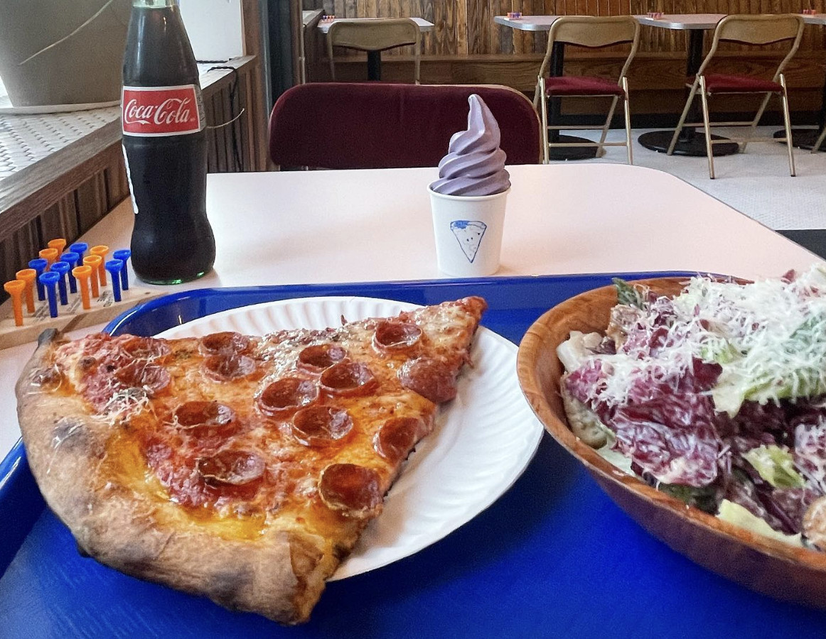 A slice of pepperoni pizza beside a salad, bottled Coke, and ice cream softie.
