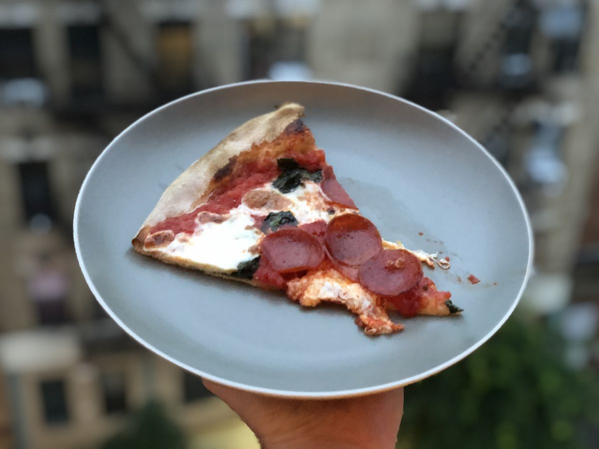 A hand holding a slice of pepperoni pizza placed in a gray plate