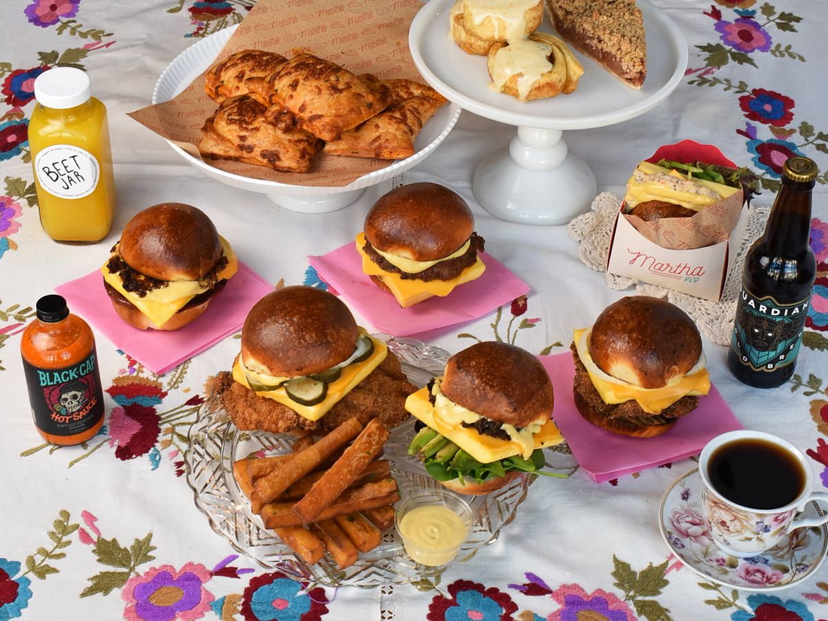 A tablescape of burgers, sandwiches, fries, beverages, and other items on a floral tablecloth.