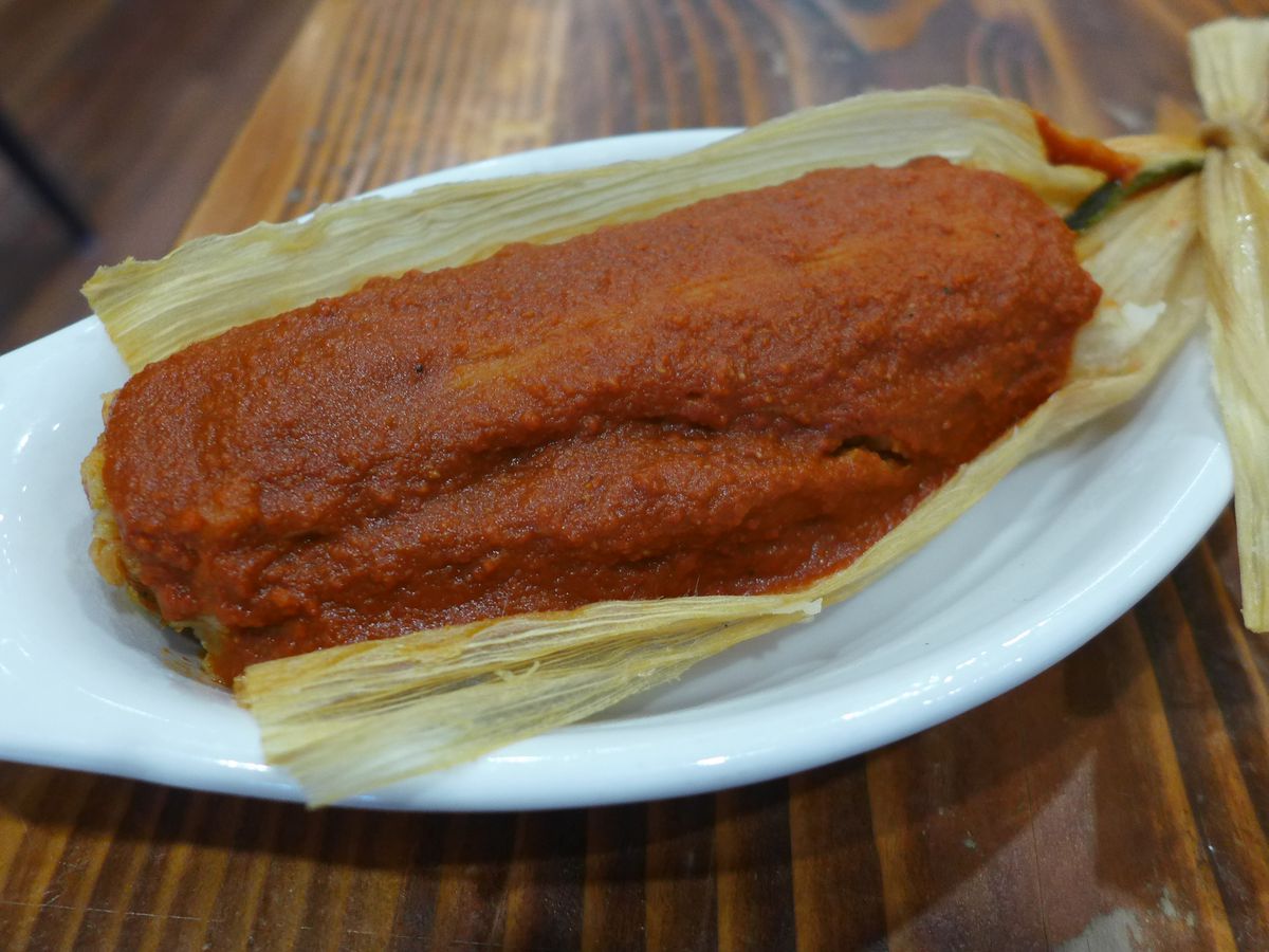 A tamale in a corn husk smothered in red gravy.