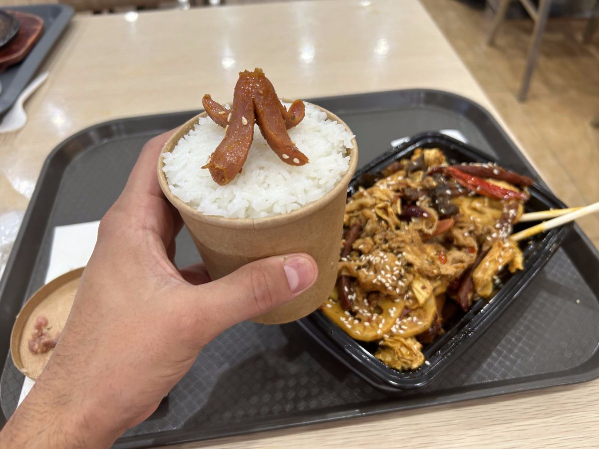 A hand holds a cup of white rice with a hot dog cut to look like an octopus.