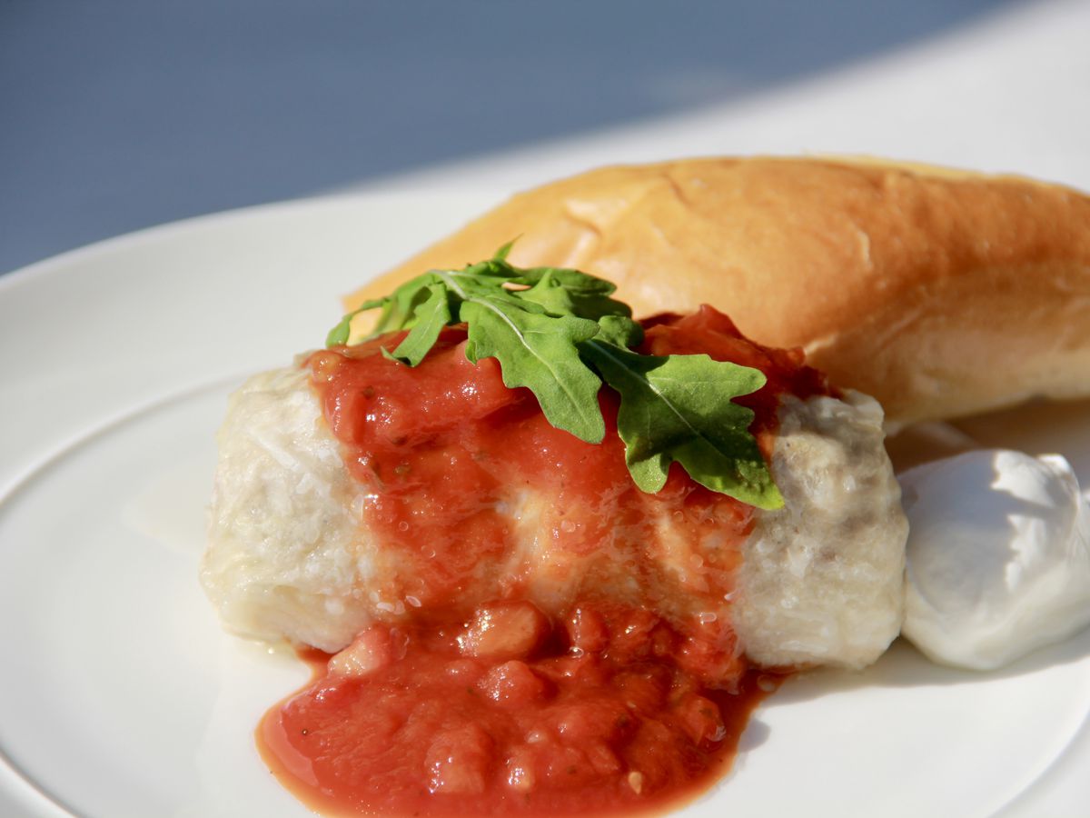 Bright red tomato sauce over a translucent roll of cooked cabbage with a white roll of bread in the background