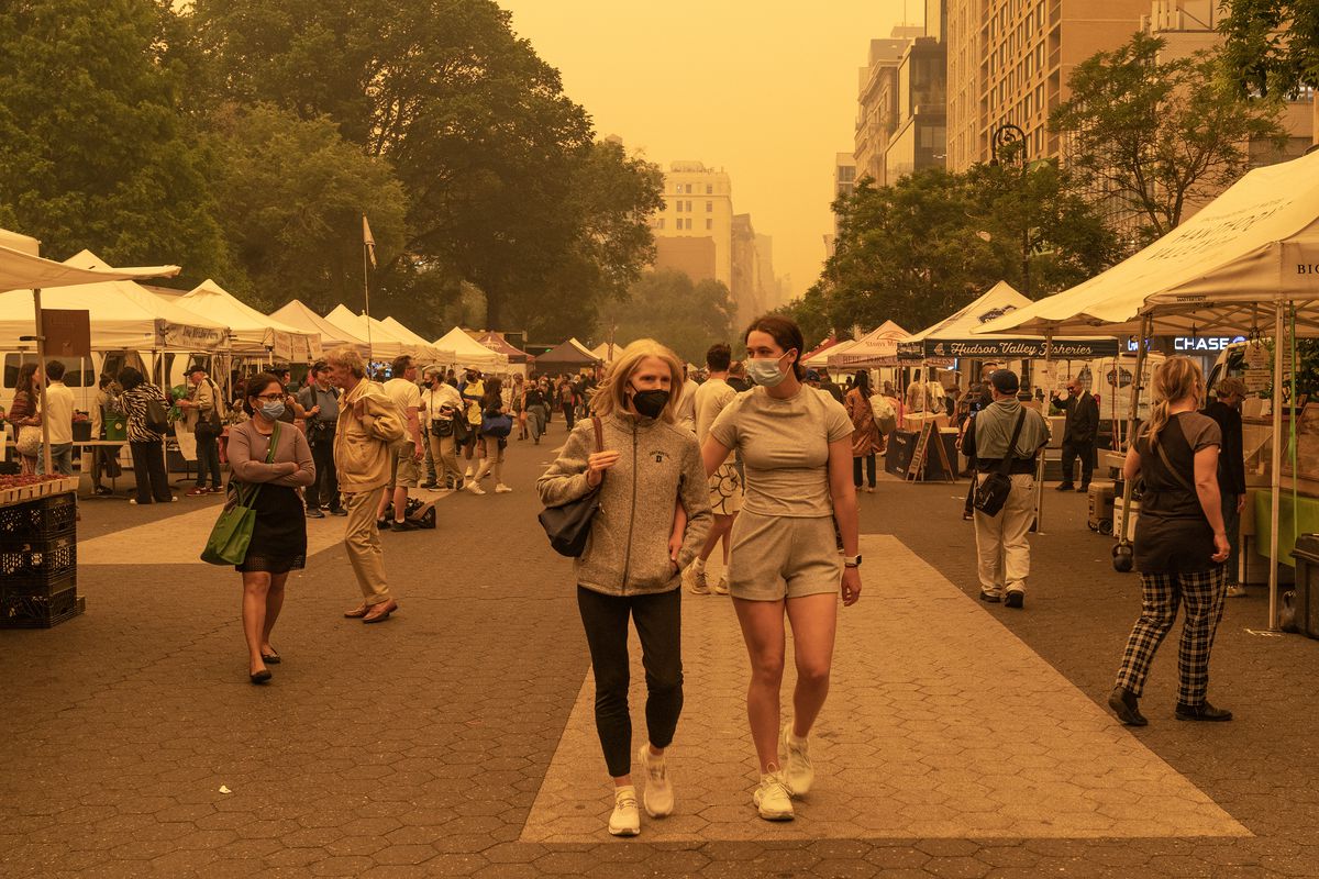 People wear face masks on June 7, 2023, walking down a street in New York City, their surroundings hazed in orange by smoke from Canadian wildfires.