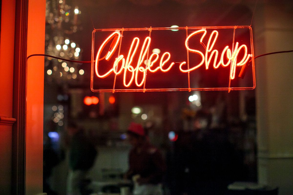 A red neon sign reading “Coffee Shop” in cursive in a store window.